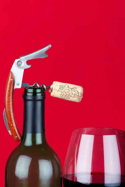 Um saca-rolhas com cortiça no topo do gargalo ao lado de um copo de vinho tinto — Fotografia de Stock