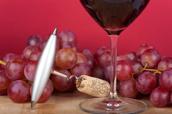 Metal corkscrew with cork lying in front of a glass of red wine — Stock Photo, Image