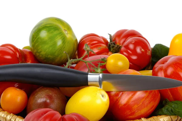 Muitos tomates orgânicos em uma cesta com uma faca na frente do fundo branco — Fotografia de Stock