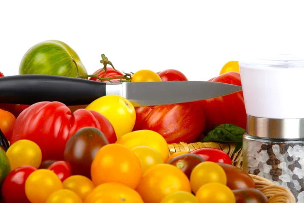 Muchos tomates orgánicos en una canasta con un cuchillo y un molino de sal y pimienta — Foto de Stock