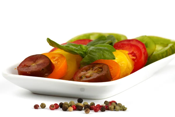 Diferentes variedades de rodajas de tomate orgánico en un plato frente al fondo blanco — Foto de Stock