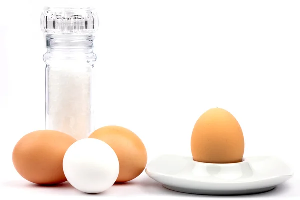 Три куриных яйца и яичные чашки с соляной мельницей — стоковое фото