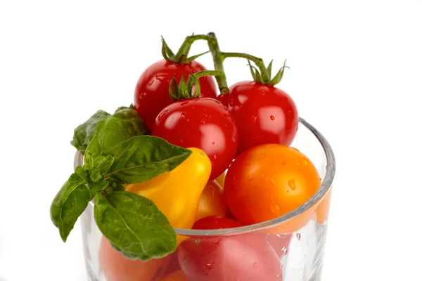 Un bicchiere pieno di piccoli pomodori biologici colorati davanti allo sfondo bianco — Foto Stock