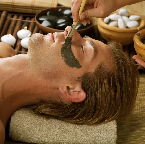 Een spa. Knappe man met een moddermasker op zijn gezicht — Stockfoto