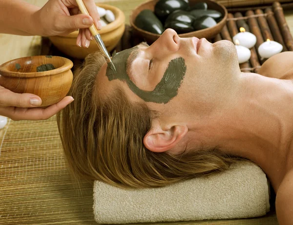 Een spa. Knappe man met een moddermasker op zijn gezicht — Stockfoto