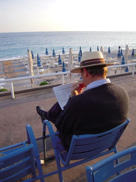 Человек, читающий газеты на синем стуле у моря — стоковое фото
