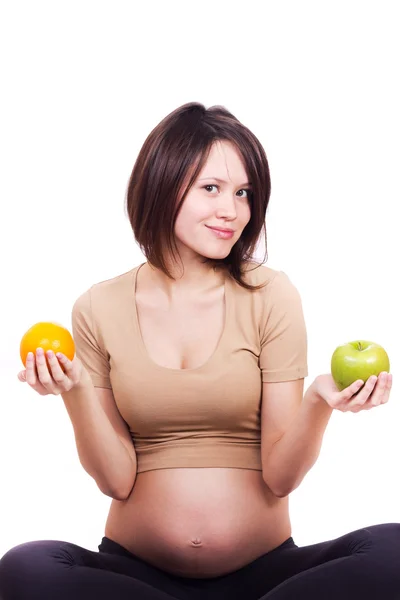 Pregnant woman holding an orange and an apple in her hands — Stock Photo, Image