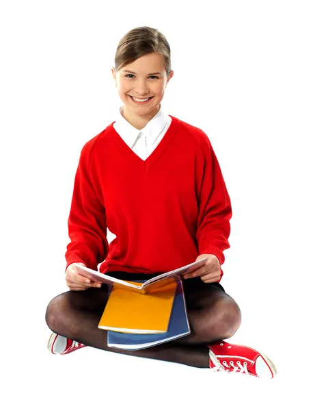 Jolie écolière assise sur le sol, tenant un livre — Photo