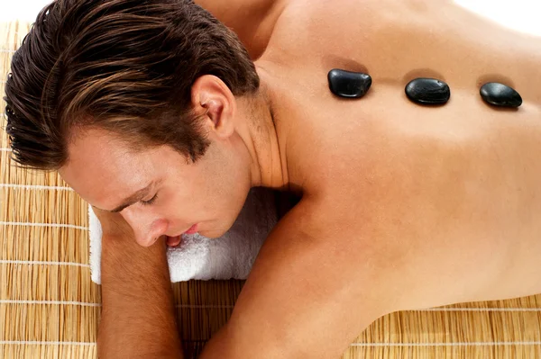 Мужчина отдыхает на массажной кровати с горячими камнями — стоковое фото