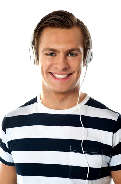 Smiling young man listening to music through headphones — Stock Photo, Image