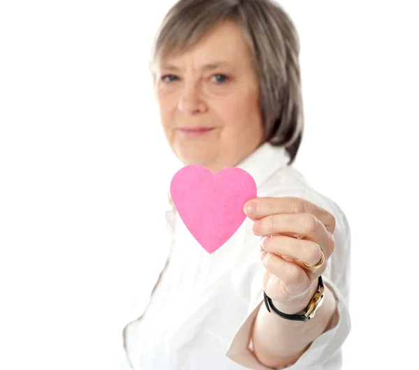 Focus on pink paper heart. Aged woman holding it — Stock Photo, Image