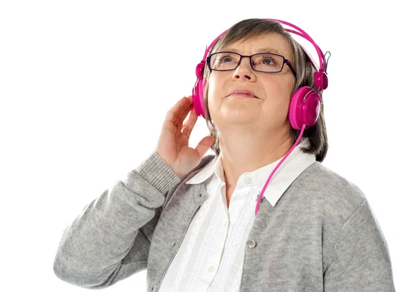Vanha nainen katselee ylös, eksyksissä musiikkimaailmassa — kuvapankkivalokuva