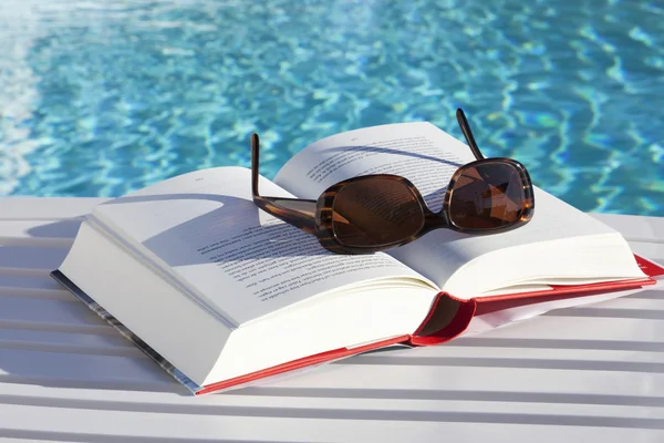 上一本书的游泳池的太阳镜 免版税图库照片