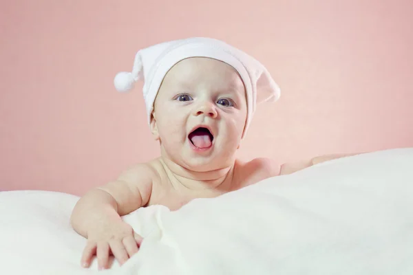 Cute laughing little baby in white hat lying down on white blank — Stock Photo, Image