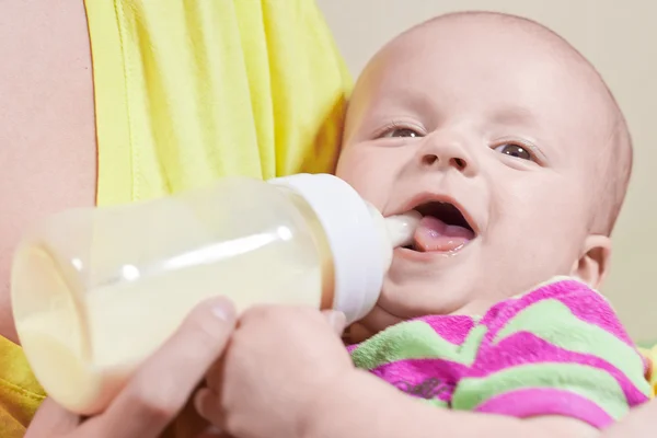 Pequeño bebé sonriente y biberón en las manos de su madre — Foto de Stock