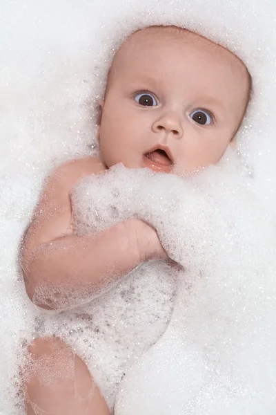 Pequeno bebê tendo um banho e deitado em espuma branca — Fotografia de Stock