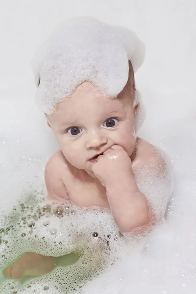Маленька дитина приймає ванну і сидить у білій піні — стокове фото
