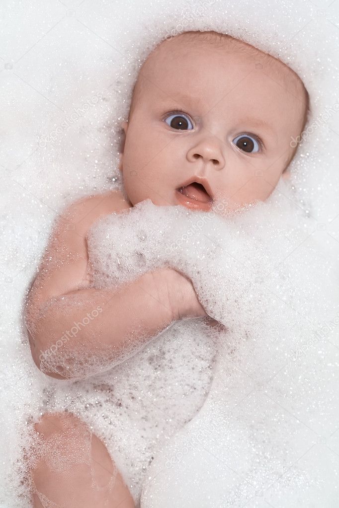 Little baby having a bath and lying in white foam