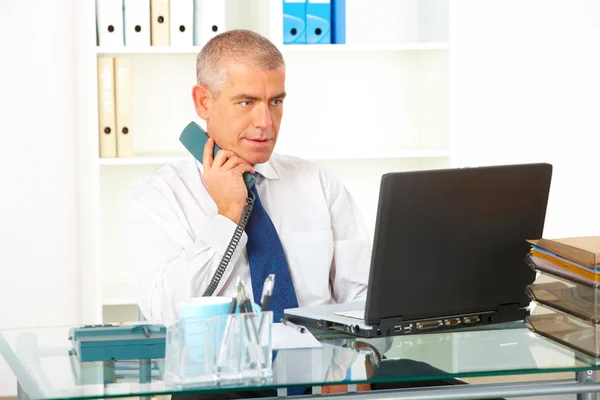 Affärsman med fast telefon tittar på laptop — Stockfoto