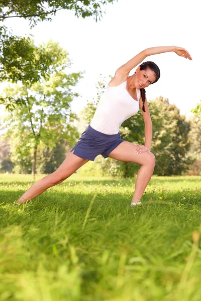 Jovem mulher fazendo exercício de alongamento na grama verde — Fotografia de Stock