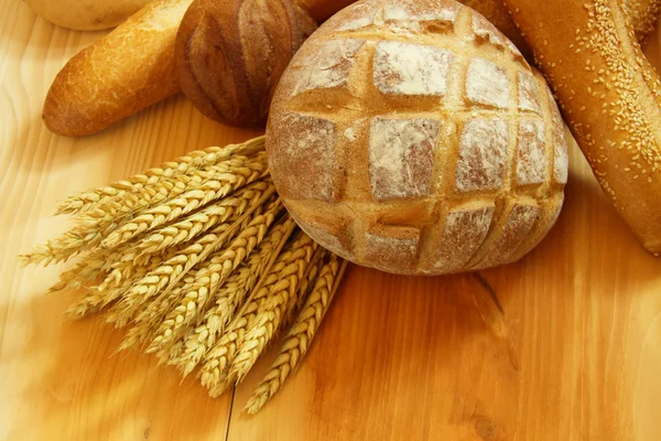 Pan surtido en mesa de madera con trigo crudo —  Fotos de Stock