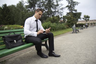 Young business man sitting on a bench clipart