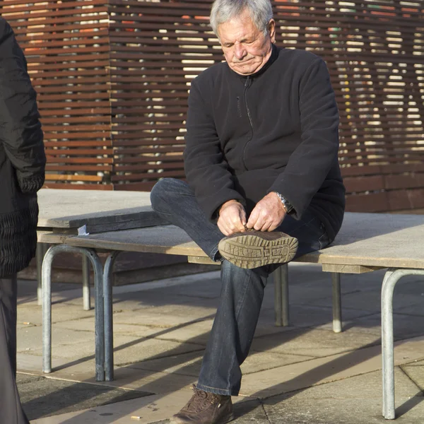 Älterer Mann sitzt auf einer Bank und bindet Schuhe, — Stockfoto