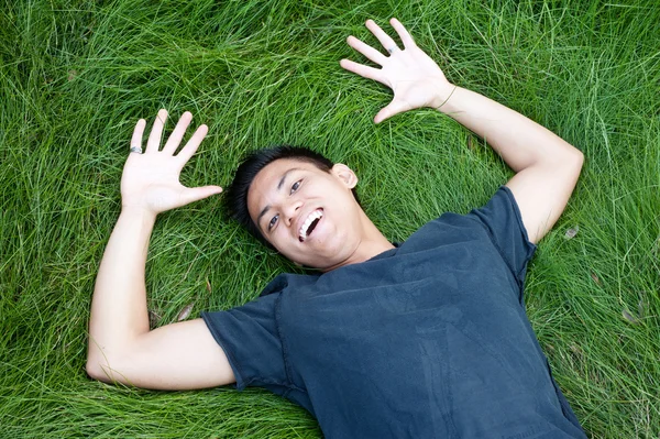 Jovem masculino asiático estudante deitado no o grama — Fotografia de Stock