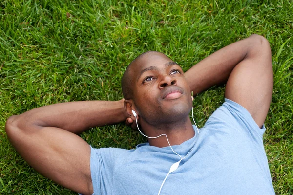 Афроамериканец, лежащий на траве и слушающий музыку — стоковое фото