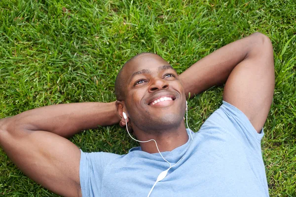 Uomo afroamericano sdraiato nell'erba ad ascoltare musica Foto Stock Royalty Free