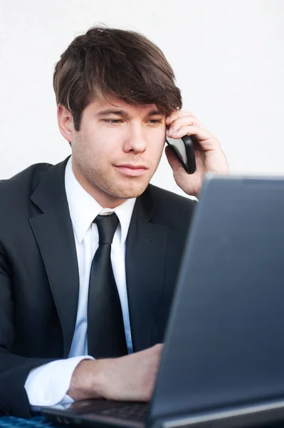 Молодой бизнесмен на ноутбуке разговаривает по телефону — стоковое фото