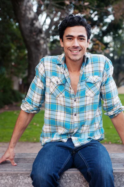 Happy young man sitting in a park — Stock Photo, Image