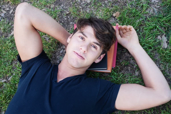 Ung manlig student liggande på gräs med böcker — Stockfoto
