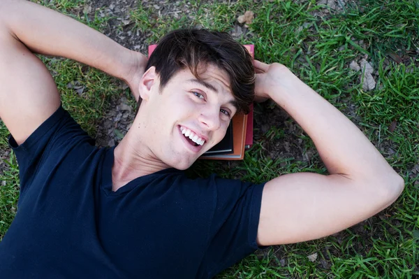 Junge männliche Studentin liegt mit Büchern im Gras — Stockfoto