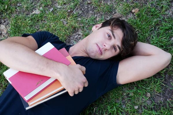Jeune étudiant homme couché sur l'herbe avec des livres — Photo