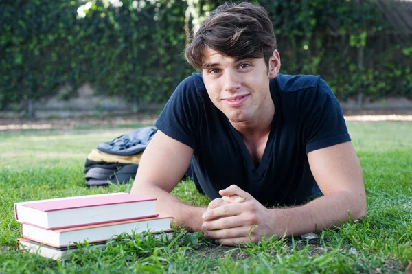 Mladý muž student ležící na trávě s knihami — Stock fotografie
