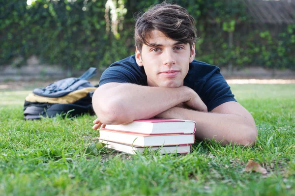 Młody student mężczyzna leżąc na trawie z książki — Zdjęcie stockowe