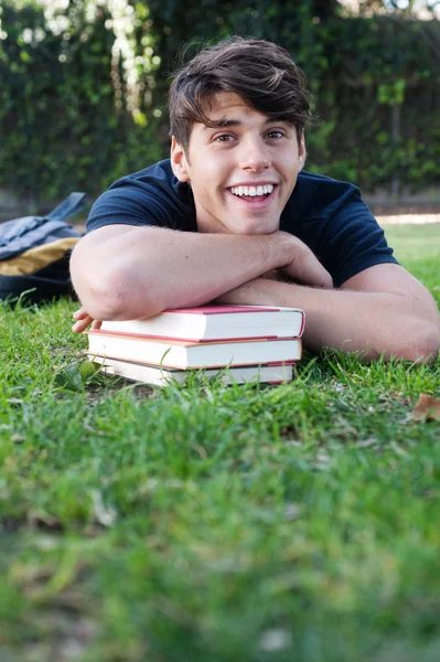 Νεαρός άνδρας των φοιτητών που ξαπλωμένος στο γρασίδι με βιβλία — Φωτογραφία Αρχείου