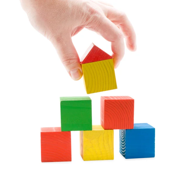 Hand establishes toy house on the wooden cubes pyramid — Stock Photo, Image