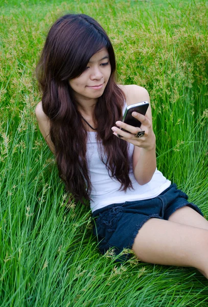 Asian cute girl texting on meadow — Stock Photo, Image