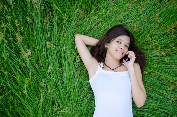 Ασιατικό κορίτσι στο τηλέφωνο που βρίσκεται σε ένα λιβάδι — Φωτογραφία Αρχείου