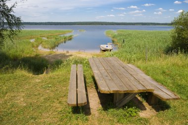 Wooden table with benches on the shore of lake clipart