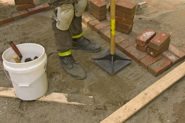 Worker tamping sand for brick laying