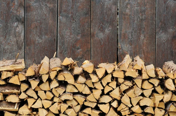 Lovely background image featuring firewood against an olden wooden wall — Stock Photo, Image