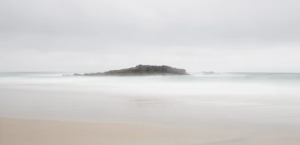 Playa en un día de niebla con una isla rocosa en el medio . — Foto de Stock