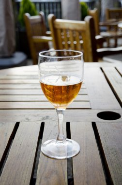 Glass of beer on a wooden table on an outdoor patio clipart