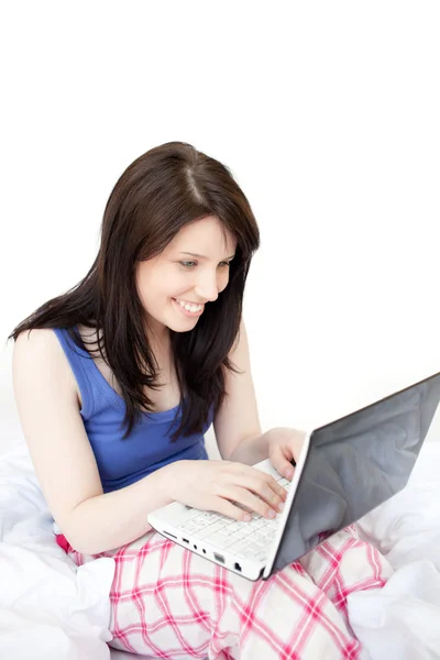 Смеющаяся женщина с помощью ноутбука, сидящего на кровати — стоковое фото
