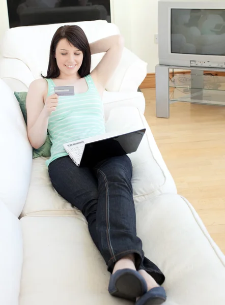 Молодая женщина делает покупки он-лайн лежа на диване — стоковое фото