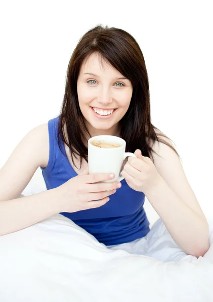 Щаслива жінка п'є каву, сидячи на ліжку — стокове фото