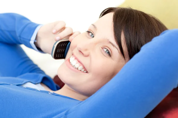 Радостная молодая женщина разговаривает по телефону лежа на диване — стоковое фото